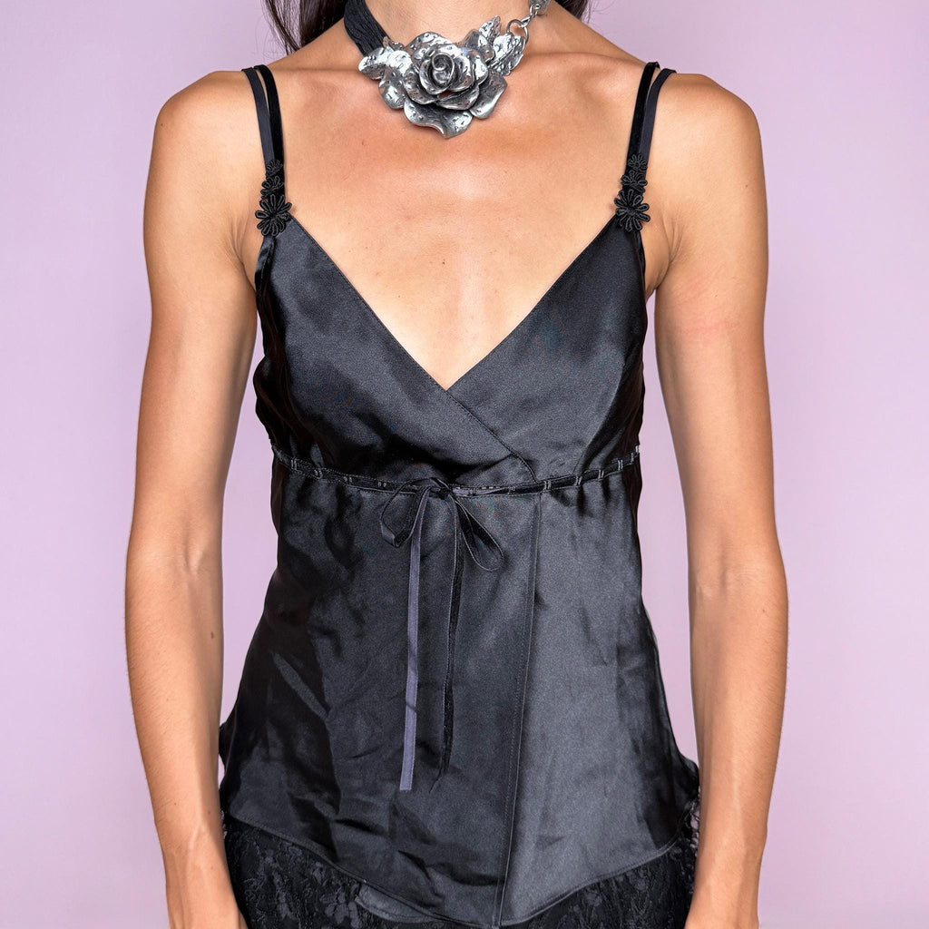 Vintage 2000s black lingerie-inspired cami top featuring a sleek satin-effect finish, deep wrap V-neckline, and delicate floral appliqué details at the straps. Designed with a fitted empire-style silhouette and a slim tie belt at the waist for a softly feminine Y2K boudoir look. Non-stretch. The composition label is missing, so the exact fabric content is unknown. From a French brand. Excellent vintage condition.