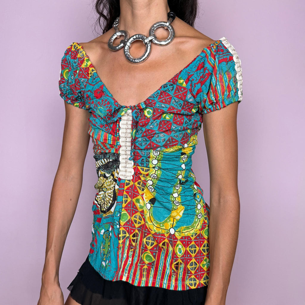 Vintage 2000s bold graphic top by Italian label Save the Queen, featuring a vivid maximalist print in turquoise, red, yellow, and green, with puffed short sleeves, a plunging V-neckline, tie-front detail, and a dramatic open split through the front. The fitted silhouette, mixed graphic motifs, and patchwork-like print give it a distinctly Y2K art-to-wear feel. Made in Italy from stretchy 100% polyester. Excellent vintage condition.