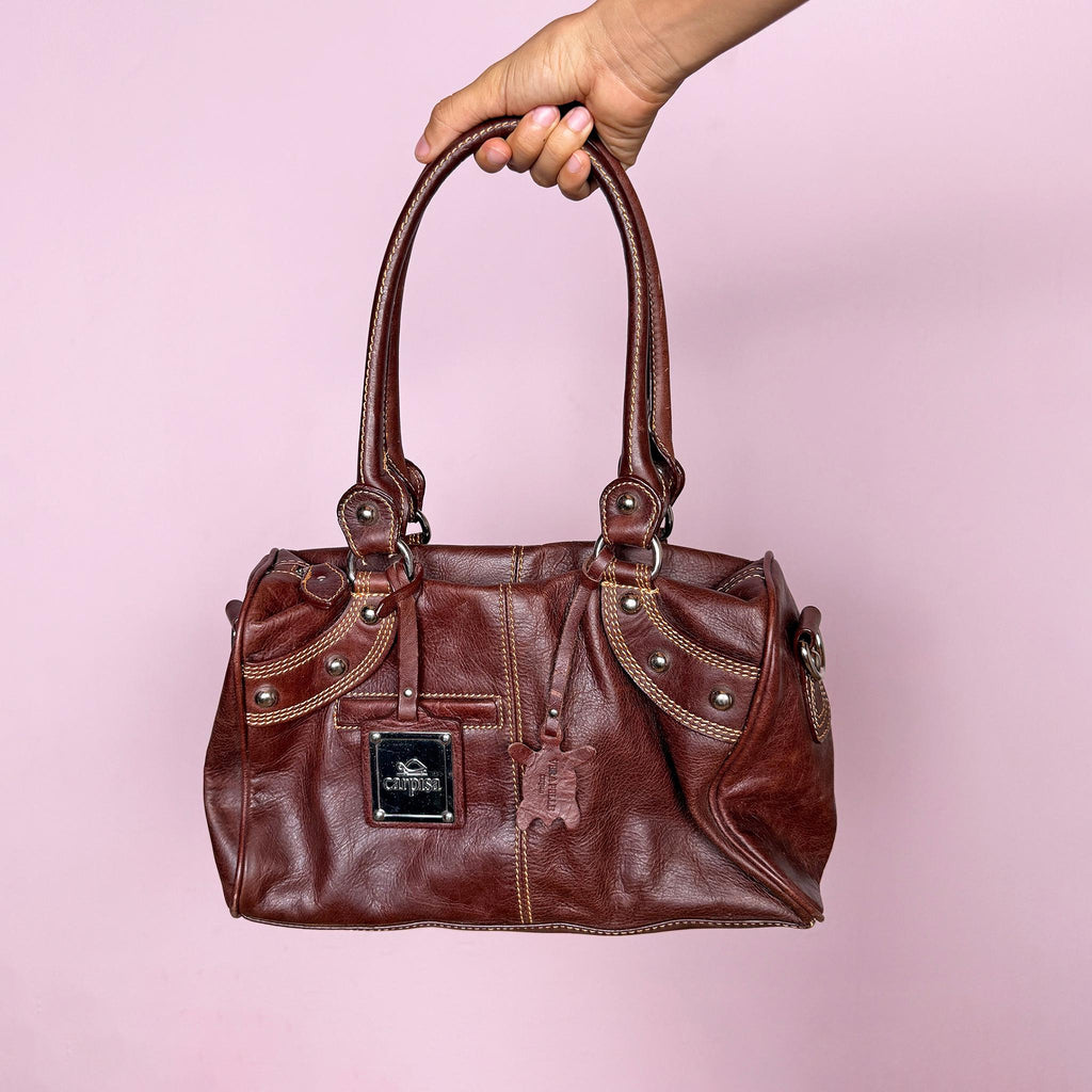 Vintage 2000s brown leather handbag crafted from genuine leather and tagged “Vera Pelle.” Features a structured rectangular silhouette, double shoulder straps, contrast topstitching, and silver-tone stud hardware. Finished with a top zip closure, branded metal plaque, and leather logo charm. From an Italian brand. Excellent vintage condition.
