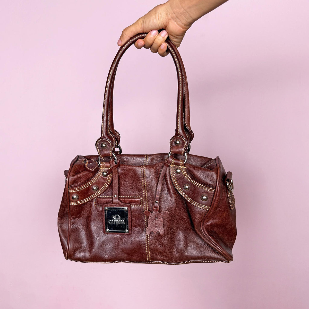 Vintage 2000s brown leather handbag crafted from genuine leather and tagged “Vera Pelle.” Features a structured rectangular silhouette, double shoulder straps, contrast topstitching, and silver-tone stud hardware. Finished with a top zip closure, branded metal plaque, and leather logo charm. From an Italian brand. Excellent vintage condition.