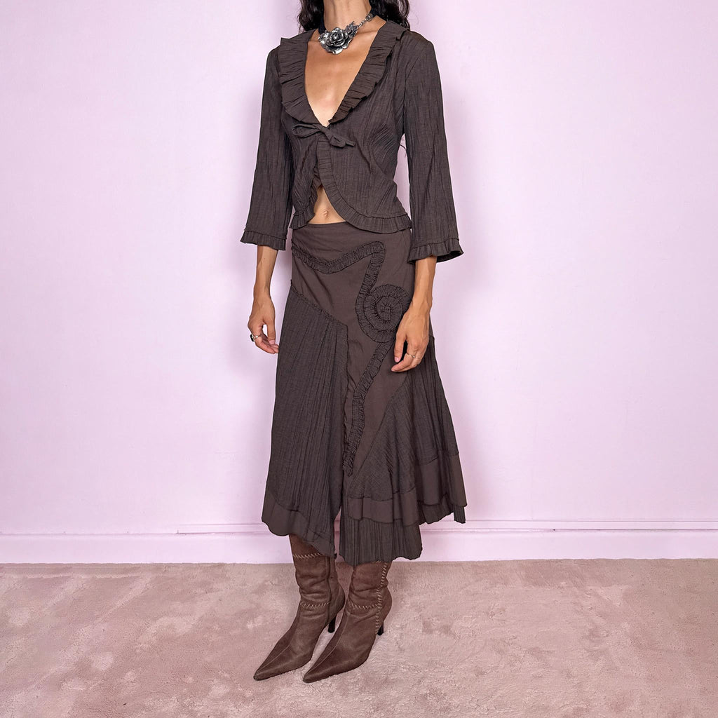 Vintage 2000s brown two-piece set featuring a fitted tie-front top with softly flared 3/4 sleeves and delicate ruffle trim, paired with a matching asymmetric midi skirt. The skirt combines fluid paneling, pleated inserts, ruffled appliqué detailing, and an irregular hem for a romantic deconstructed Y2K silhouette, with a side zip closure. Can be worn high-waisted for size S or slightly lower on the waist for size XS. Made from a non-stretch polyester and viscose blend.