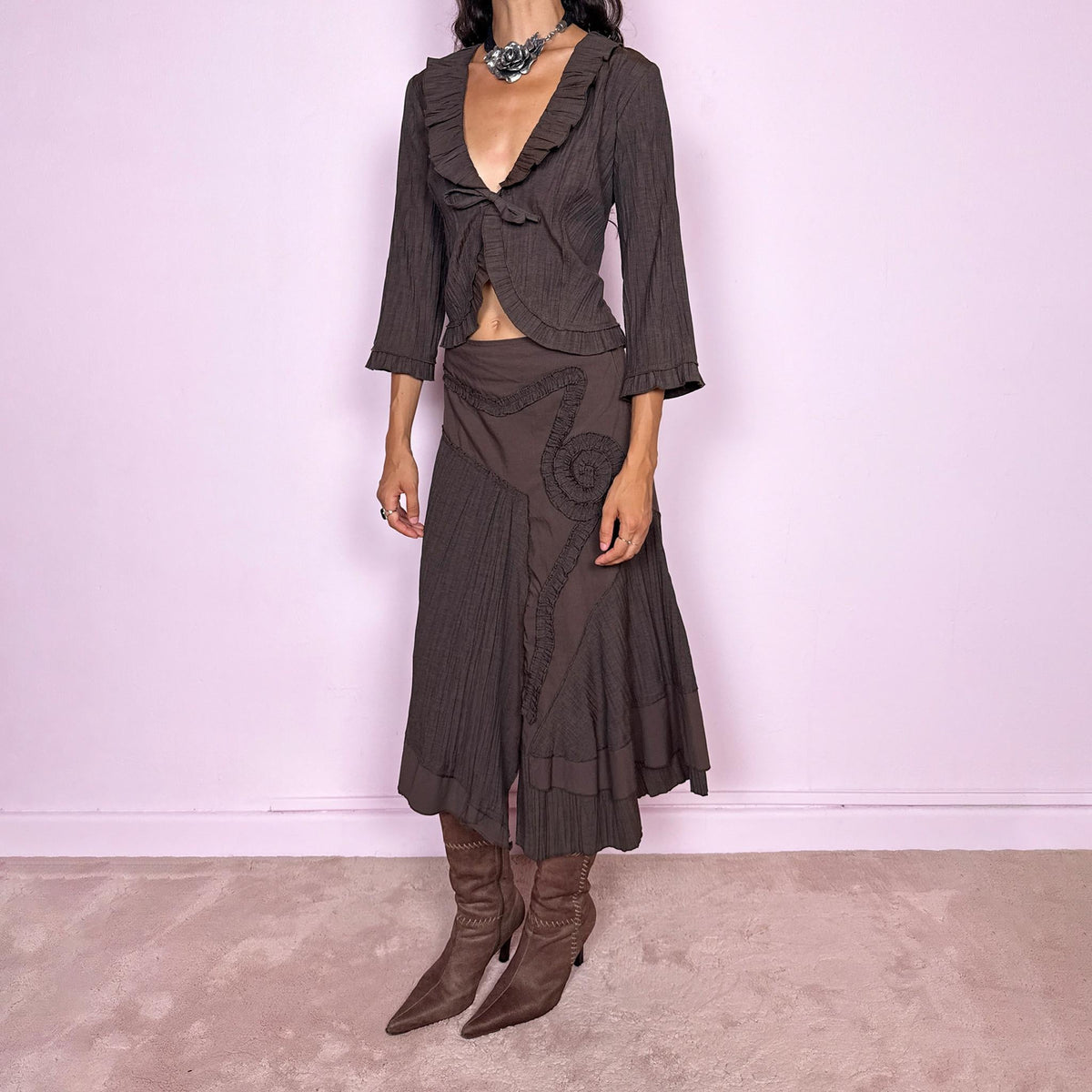Vintage 2000s brown two-piece set featuring a fitted tie-front top with softly flared 3/4 sleeves and delicate ruffle trim, paired with a matching asymmetric midi skirt. The skirt combines fluid paneling, pleated inserts, ruffled appliqué detailing, and an irregular hem for a romantic deconstructed Y2K silhouette, with a side zip closure. Can be worn high-waisted for size S or slightly lower on the waist for size XS. Made from a non-stretch polyester and viscose blend.