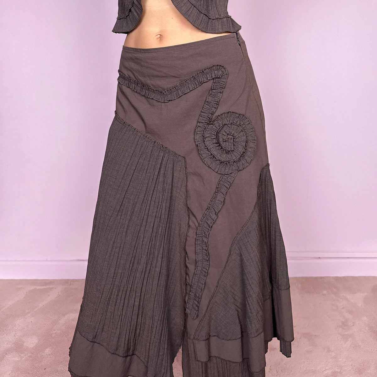 Vintage 2000s brown two-piece set featuring a fitted tie-front top with softly flared 3/4 sleeves and delicate ruffle trim, paired with a matching asymmetric midi skirt. The skirt combines fluid paneling, pleated inserts, ruffled appliqué detailing, and an irregular hem for a romantic deconstructed Y2K silhouette, with a side zip closure. Can be worn high-waisted for size S or slightly lower on the waist for size XS. Made from a non-stretch polyester and viscose blend.