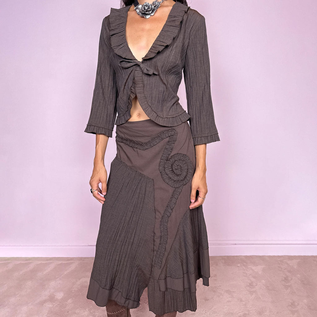 Vintage 2000s brown two-piece set featuring a fitted tie-front top with softly flared 3/4 sleeves and delicate ruffle trim, paired with a matching asymmetric midi skirt. The skirt combines fluid paneling, pleated inserts, ruffled appliqué detailing, and an irregular hem for a romantic deconstructed Y2K silhouette, with a side zip closure. Can be worn high-waisted for size S or slightly lower on the waist for size XS. Made from a non-stretch polyester and viscose blend.