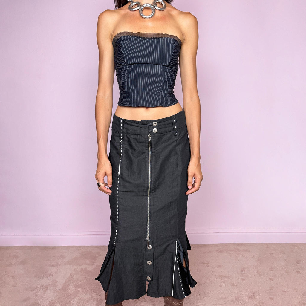 Vintage 2000s black midi skirt featuring an exposed full-length front zip, double-button waistband, and contrast white stitching throughout. The lower section opens into sculptural deconstructed panels with additional button and zip detailing, creating an asymmetric, utilitarian avant-garde feel. Can be worn high-waisted for size M or slightly lower on the waist for sizes S and XS. Non-stretch. Made in Holland by a Dutch brand from a structured blend of 52% cotton and 48% linen
