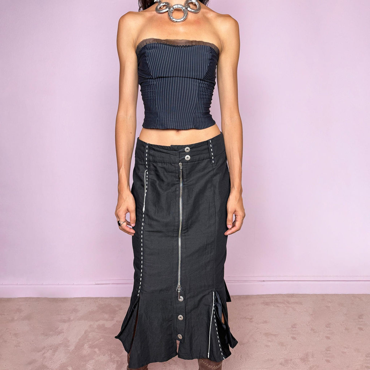 Vintage 2000s black midi skirt featuring an exposed full-length front zip, double-button waistband, and contrast white stitching throughout. The lower section opens into sculptural deconstructed panels with additional button and zip detailing, creating an asymmetric, utilitarian avant-garde feel. Can be worn high-waisted for size M or slightly lower on the waist for sizes S and XS. Non-stretch. Made in Holland by a Dutch brand from a structured blend of 52% cotton and 48% linen