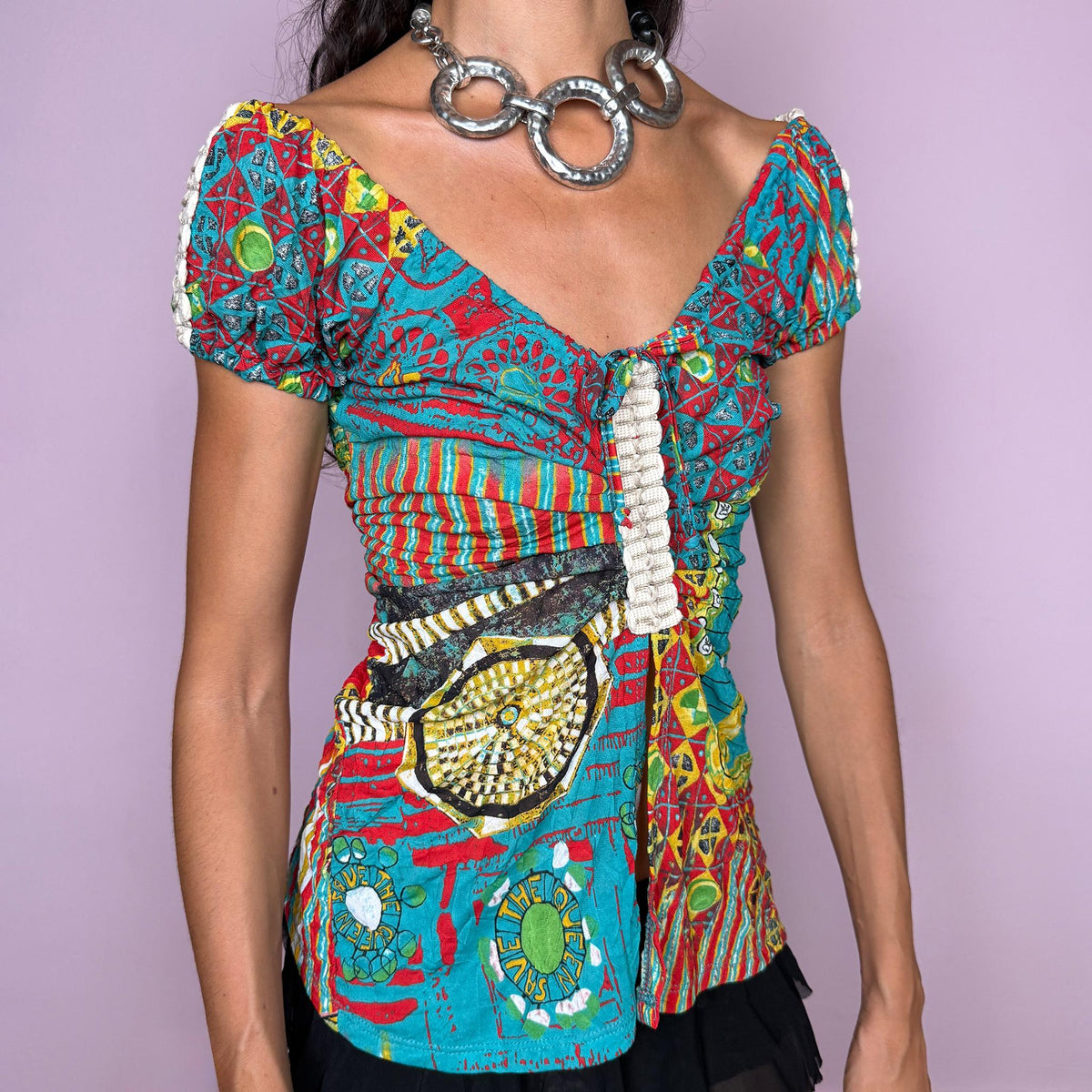 Vintage 2000s bold graphic top by Italian label Save the Queen, featuring a vivid maximalist print in turquoise, red, yellow, and green, with puffed short sleeves, a plunging V-neckline, tie-front detail, and a dramatic open split through the front. The fitted silhouette, mixed graphic motifs, and patchwork-like print give it a distinctly Y2K art-to-wear feel. Made in Italy from stretchy 100% polyester. Excellent vintage condition.