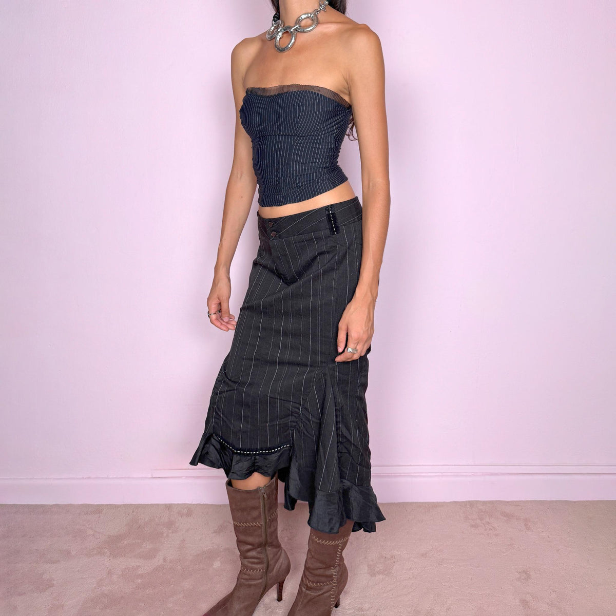 Vintage 2000s black pinstripe midi skirt featuring a fitted low-rise silhouette with a diagonal waistband construction, front zip closure, vertical pinstripes, and sculptural paneling through the lower skirt. Finished with an asymmetric flared hem and contrasting satin-like ruffle trim for a dramatic, deconstructed Y2K silhouette. Made in Italy by an Italian brand from a slightly stretchy blend of 62% polyester, 33% viscose, and 5% elastane. Excellent vintage condition.