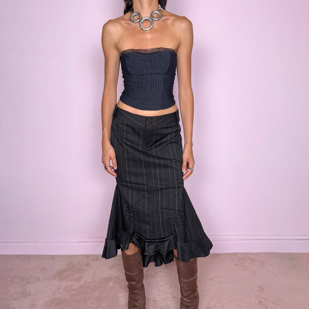 Vintage 2000s black pinstripe midi skirt featuring a fitted low-rise silhouette with a diagonal waistband construction, front zip closure, vertical pinstripes, and sculptural paneling through the lower skirt. Finished with an asymmetric flared hem and contrasting satin-like ruffle trim for a dramatic, deconstructed Y2K silhouette. Made in Italy by an Italian brand from a slightly stretchy blend of 62% polyester, 33% viscose, and 5% elastane. Excellent vintage condition.