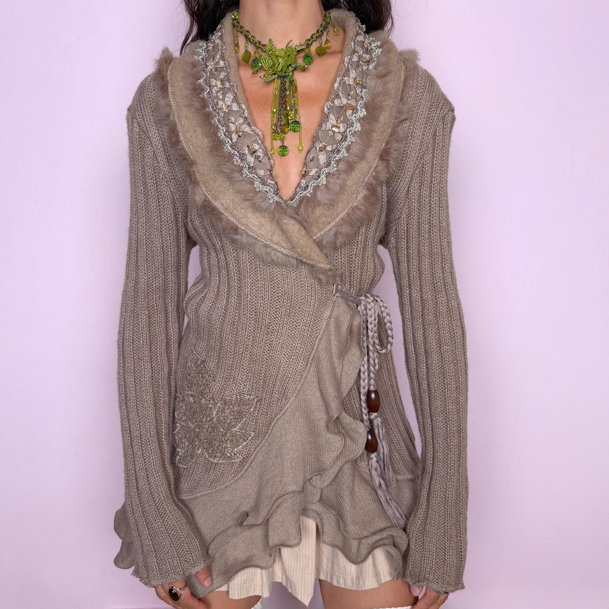 Vintage 2000s taupe-brown wrap cardigan crafted from a soft blend of 30% mohair, 20% wool, and 50% acrylic. Featuring a ribbed knit body, wrap-front silhouette with a braided tie fastening and wooden bead details, layered ruffle trim along the lower front, textured embroidery, and a plush faux-fur-trimmed shawl collar with beaded detailing. Excellent vintage condition.