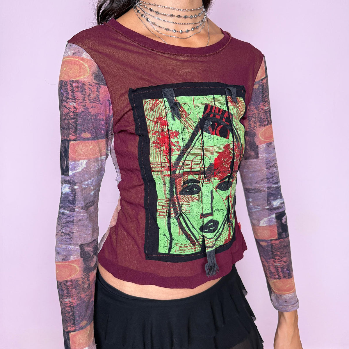 Vintage 2000s deconstructed graphic mesh top featuring a fitted burgundy body with contrasting printed long sleeves and a bold mixed-media face graphic appliqué at the front, finished with raw-edge fabric tabs and layered textile detailing. The combination of mesh, painterly print, and exposed appliqué construction gives it an art-to-wear, avant-garde aesthetic. From a French brand, made in France from stretchy 100% polyamide. Great vintage condition.