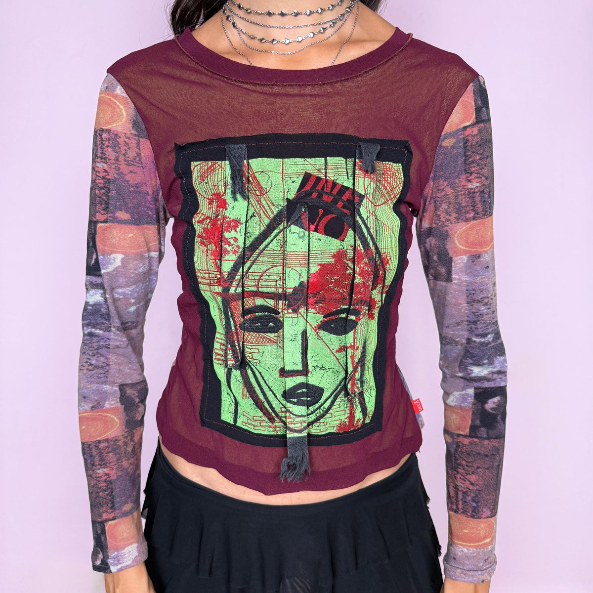 Vintage 2000s deconstructed graphic mesh top featuring a fitted burgundy body with contrasting printed long sleeves and a bold mixed-media face graphic appliqué at the front, finished with raw-edge fabric tabs and layered textile detailing. The combination of mesh, painterly print, and exposed appliqué construction gives it an art-to-wear, avant-garde aesthetic. From a French brand, made in France from stretchy 100% polyamide. Great vintage condition.