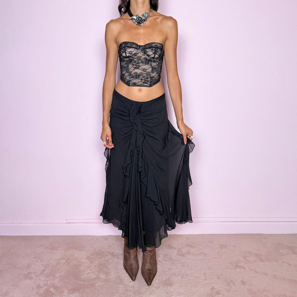 Vintage 2000s black silk midi skirt featuring soft ruching through the hips, cascading ruffle detailing down the front and sides, and a fluid flared hem for dramatic movement. Back zip closure and non-stretch. The layered silk construction and sculptural draping are ideal for elevated evening styling. Can be worn mid-rise for size M or lower on the waist for size S. Made in Italy by an Italian brand from 100% silk with a 100% polyester lining. Excellent vintage condition.
