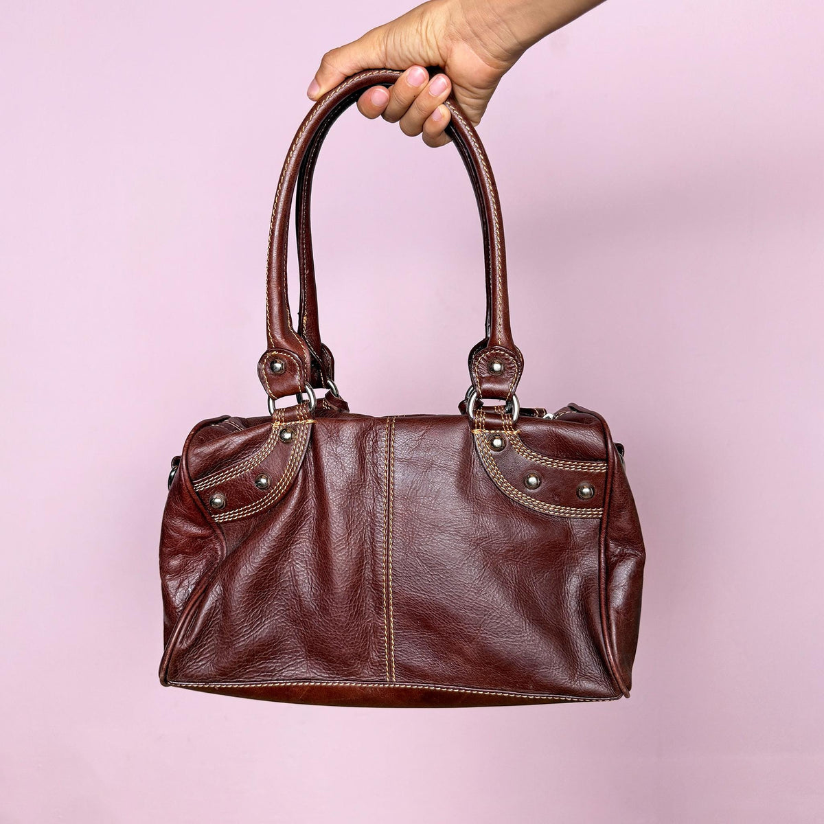 Vintage 2000s brown leather handbag crafted from genuine leather and tagged “Vera Pelle.” Features a structured rectangular silhouette, double shoulder straps, contrast topstitching, and silver-tone stud hardware. Finished with a top zip closure, branded metal plaque, and leather logo charm. From an Italian brand. Excellent vintage condition.