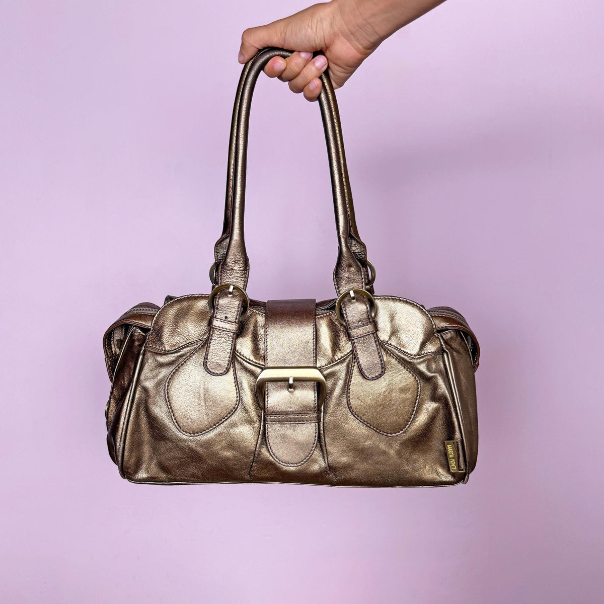 Vintage 2000s metallic bronze-gold leather handbag crafted from genuine leather. Features a structured rectangular silhouette with double shoulder straps and a statement buckle accent. Finished with a top zip closure and snap-button fastening. The warm metallic finish shifts between antique gold and bronze. From a Portuguese leather goods brand. Excellent vintage condition.