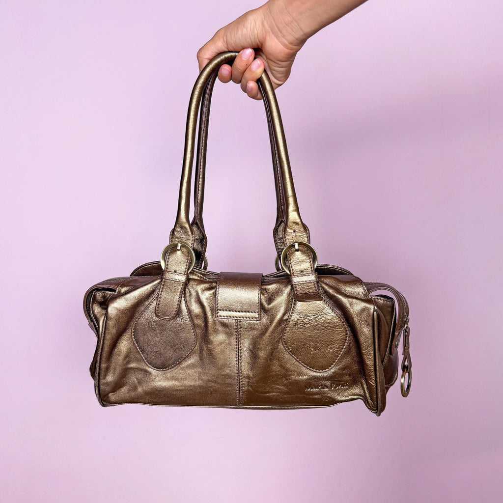Vintage 2000s metallic bronze-gold leather handbag crafted from genuine leather. Features a structured rectangular silhouette with double shoulder straps and a statement buckle accent. Finished with a top zip closure and snap-button fastening. The warm metallic finish shifts between antique gold and bronze. From a Portuguese leather goods brand. Excellent vintage condition.