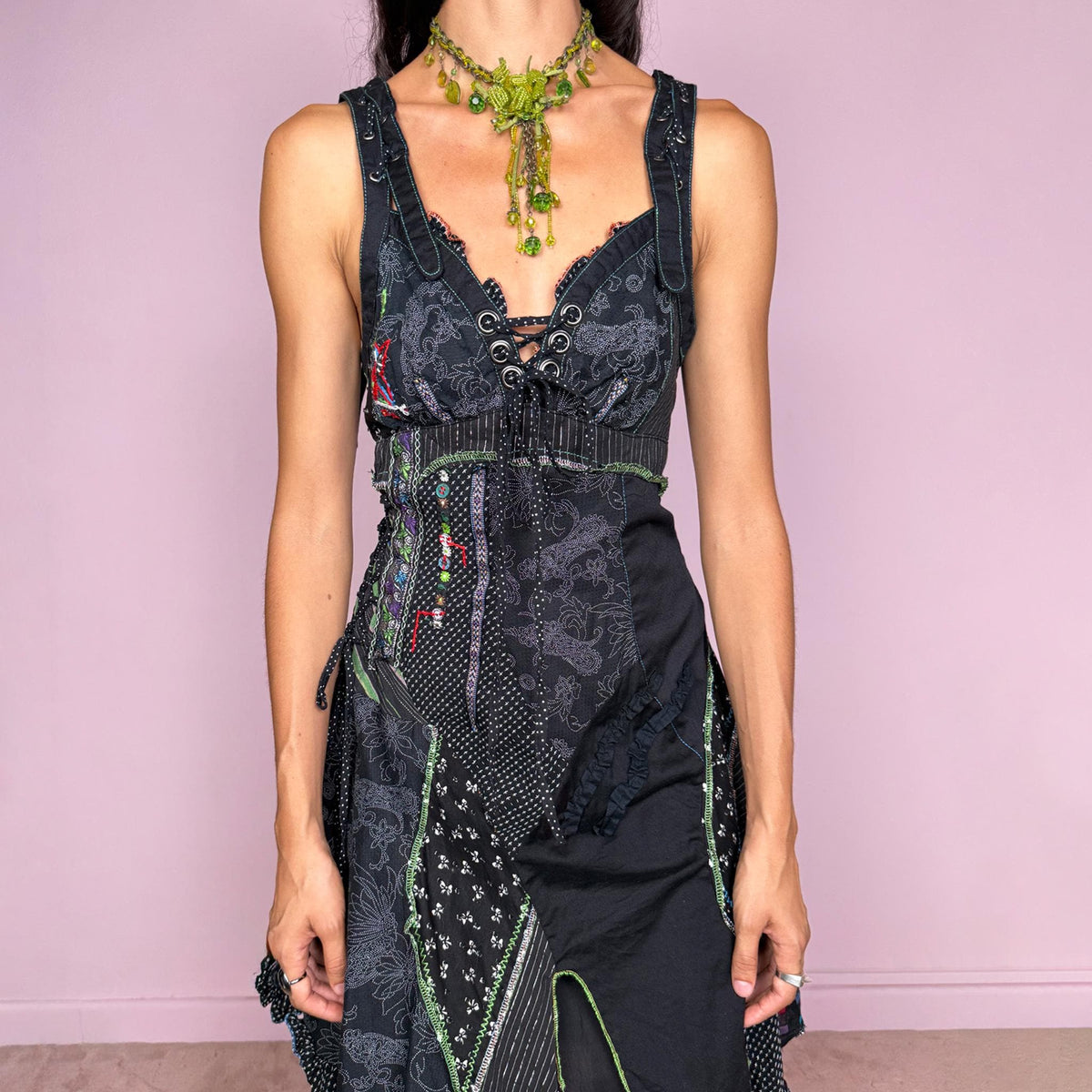 Vintage 2000s black midi dress featuring a deconstructed patchwork construction with mixed pinstripe, floral, and textured panels. Designed with a deep lace-up neckline, asymmetric layered skirt, raw-edge detailing, decorative stitching, and a dramatic draped side panel. Finished with a side zip closure. Non-stretch. The irregular construction and mixed textures are ideal for ragged-doll, avant-garde looks.