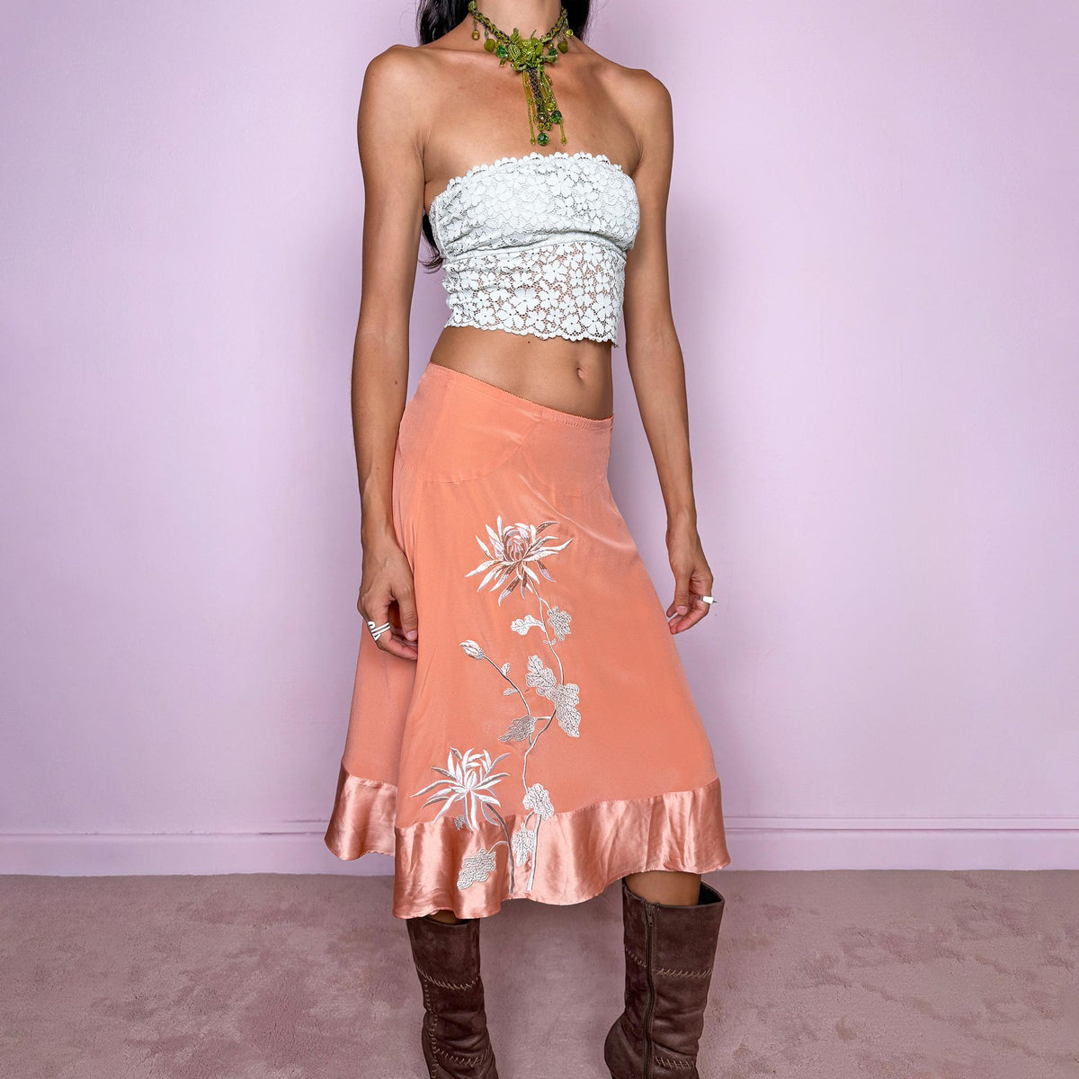 Vintage 2000s pastel salmon-orange midi skirt crafted from a fluid, non-stretch fabric with a silk-like feel, featuring delicate white floral embroidery, a flared silhouette, satin trim at the hem, and a satin lining. The soft salmon tone and botanical embroidery give it a dreamy, romantic bohemian aesthetic. The composition label is missing, so the exact fabric is unknown, though it has the look and feel of silk. From a Danish brand.