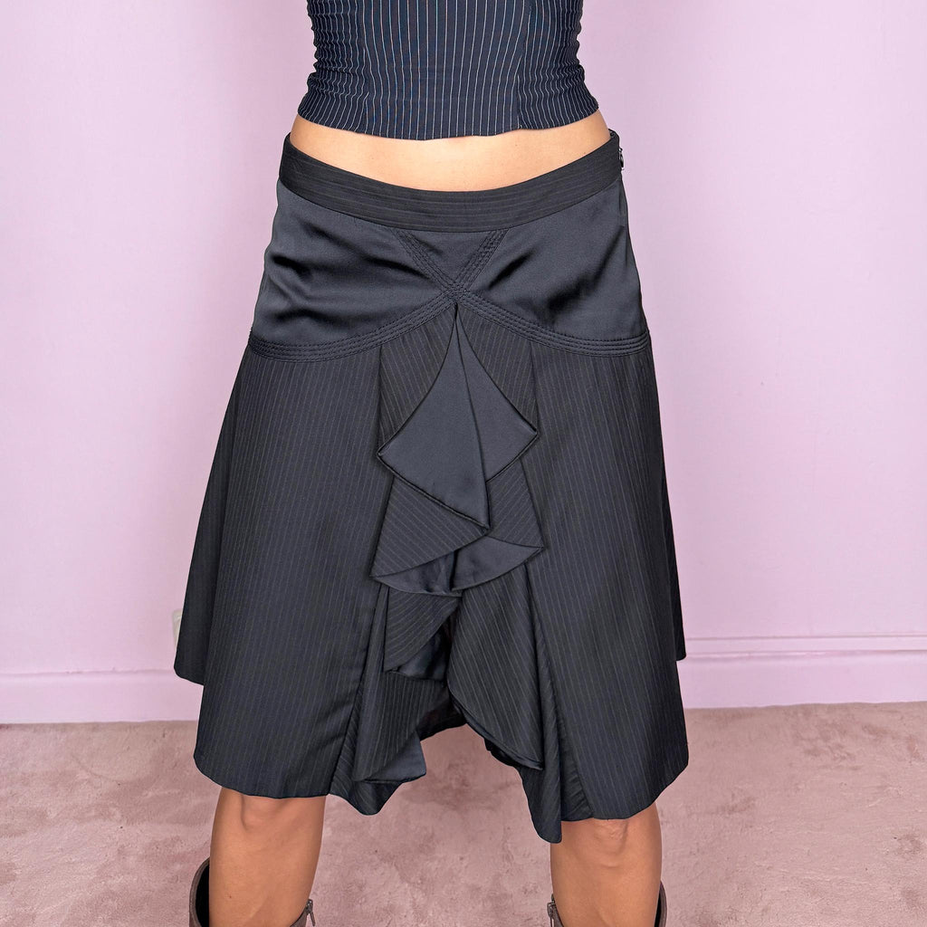 Vintage 2000s black pinstripe midi skirt featuring a side zip closure and sculptural layered panel construction with contrasting satin-like inserts and cascading asymmetric detailing through the front. Non-stretch. The mix of tailored pinstripes, curved seamwork, and deconstructed draping gives it a formal, dark avant-garde aesthetic. Can be worn mid-rise for size S or lower on the waist for size XS.