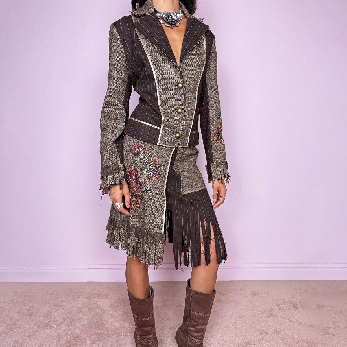 Vintage 2000s deconstructed two-piece skirt suit. The fitted jacket features mixed pinstripe and herringbone panels, raw-edge detailing, contrast piping, floral embroidery, decorative metal buttons, and pleated fringe cuffs. Paired with a matching asymmetric midi skirt featuring layered panel construction, a side zip closure, embroidered floral motifs, and dramatic cut fringe through the lower section. Non-stretch.