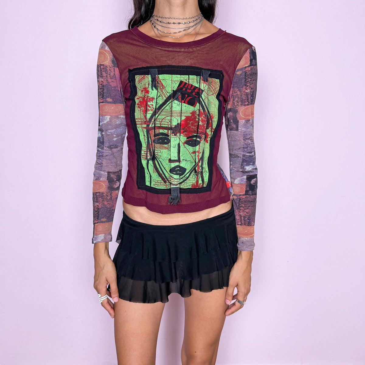 Vintage 2000s deconstructed graphic mesh top featuring a fitted burgundy body with contrasting printed long sleeves and a bold mixed-media face graphic appliqué at the front, finished with raw-edge fabric tabs and layered textile detailing. The combination of mesh, painterly print, and exposed appliqué construction gives it an art-to-wear, avant-garde aesthetic. From a French brand, made in France from stretchy 100% polyamide. Great vintage condition.