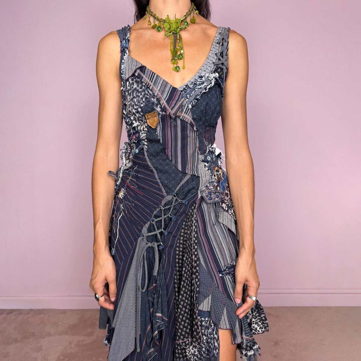 Vintage 2000s dark blue patchwork midi dress featuring an intricate deconstructed construction made from mixed pinstripe, floral, animal-print, and textured fabric panels. Designed with a deep V-neckline, fitted bodice, asymmetric layered skirt, exposed seams, raw-edge finishes, decorative stitching, lace-up detailing, and multiple draped panels throughout. Finished with a side zip closure. Non-stretch. For ragged-doll, bohemian, and avant-garde looks.