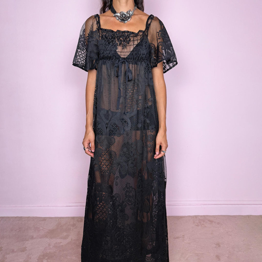 Vintage 90s black sheer lace maxi dress featuring an intricate all-over lace design with mixed floral and geometric motifs. Designed with a square neckline, softly gathered bust, short sheer sleeves, front tie detail, and a relaxed floor-length silhouette with a semi-sheer lining. For dark romantic styling and layered looks. The labels are missing, so the exact fabric is unknown. Excellent vintage condition.