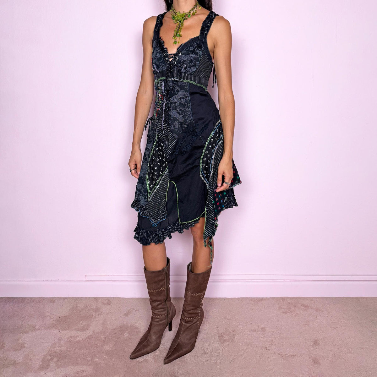Vintage 2000s black midi dress featuring a deconstructed patchwork construction with mixed pinstripe, floral, and textured panels. Designed with a deep lace-up neckline, asymmetric layered skirt, raw-edge detailing, decorative stitching, and a dramatic draped side panel. Finished with a side zip closure. Non-stretch. The irregular construction and mixed textures are ideal for ragged-doll, avant-garde looks.