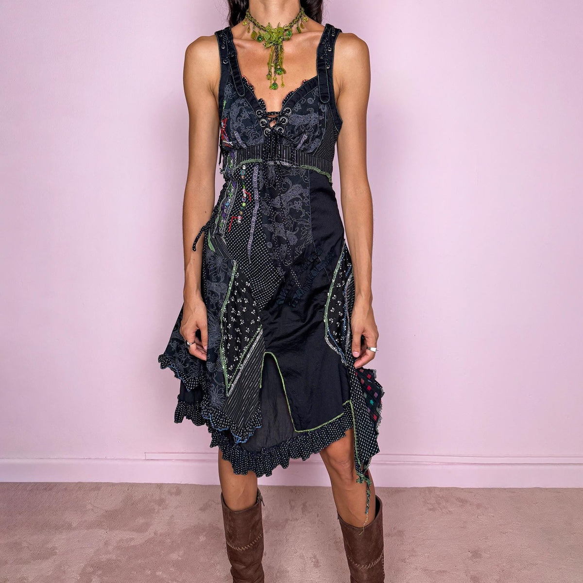 Vintage 2000s black midi dress featuring a deconstructed patchwork construction with mixed pinstripe, floral, and textured panels. Designed with a deep lace-up neckline, asymmetric layered skirt, raw-edge detailing, decorative stitching, and a dramatic draped side panel. Finished with a side zip closure. Non-stretch. The irregular construction and mixed textures are ideal for ragged-doll, avant-garde looks.