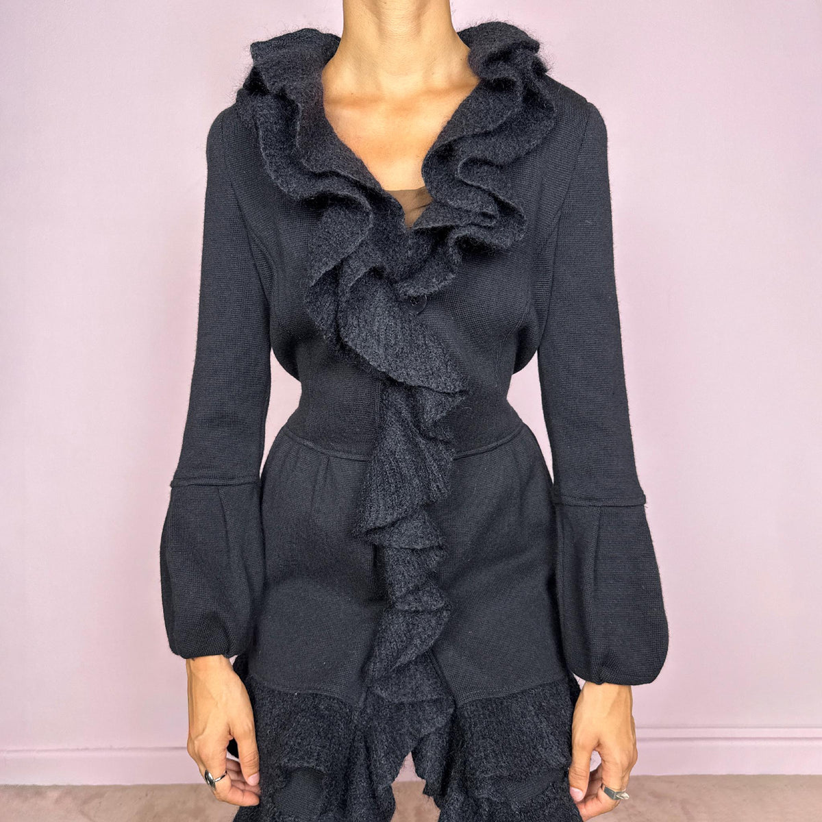 Vintage 2000s black wool coat, crafted from 100% wool with contrasting textured inserts in a blend of 50% mohair, 30% polyamide, and 20% wool. Featuring a fitted silhouette with dramatic ruffled trim through the neckline and front, voluminous sleeves, button closure, and pockets. Finished with a removable fabric belt that can be tied at the front or back to adjust the shape. From an Italian brand. Great vintage condition.