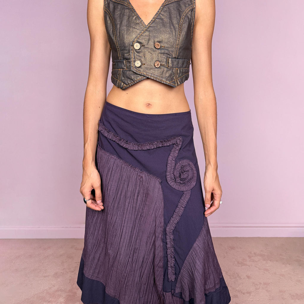Vintage 2000s dark purple asymmetric midi skirt from a French brand, made in France. Features an irregular layered silhouette with contrasting pleated panels, curved seam construction, sculptural ruffled appliqué detailing, and a layered hem. Finished with a side zip closure. Can be worn high-waisted for size L or lower on the waist for sizes M–S.