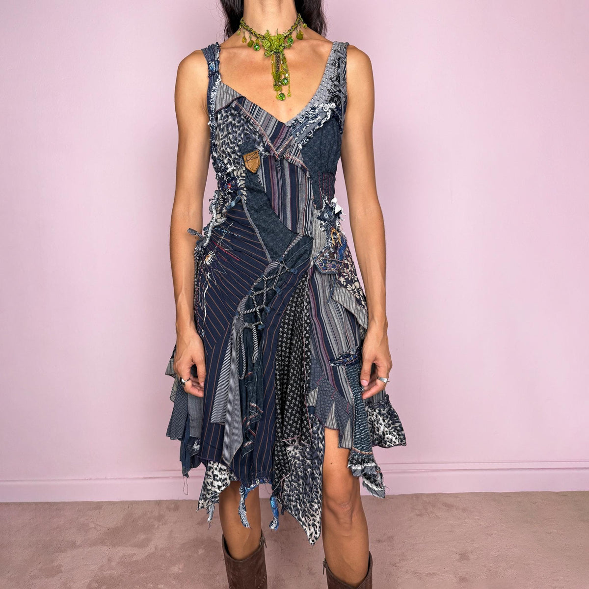 Vintage 2000s dark blue patchwork midi dress featuring an intricate deconstructed construction made from mixed pinstripe, floral, animal-print, and textured fabric panels. Designed with a deep V-neckline, fitted bodice, asymmetric layered skirt, exposed seams, raw-edge finishes, decorative stitching, lace-up detailing, and multiple draped panels throughout. Finished with a side zip closure. Non-stretch. For ragged-doll, bohemian, and avant-garde looks.