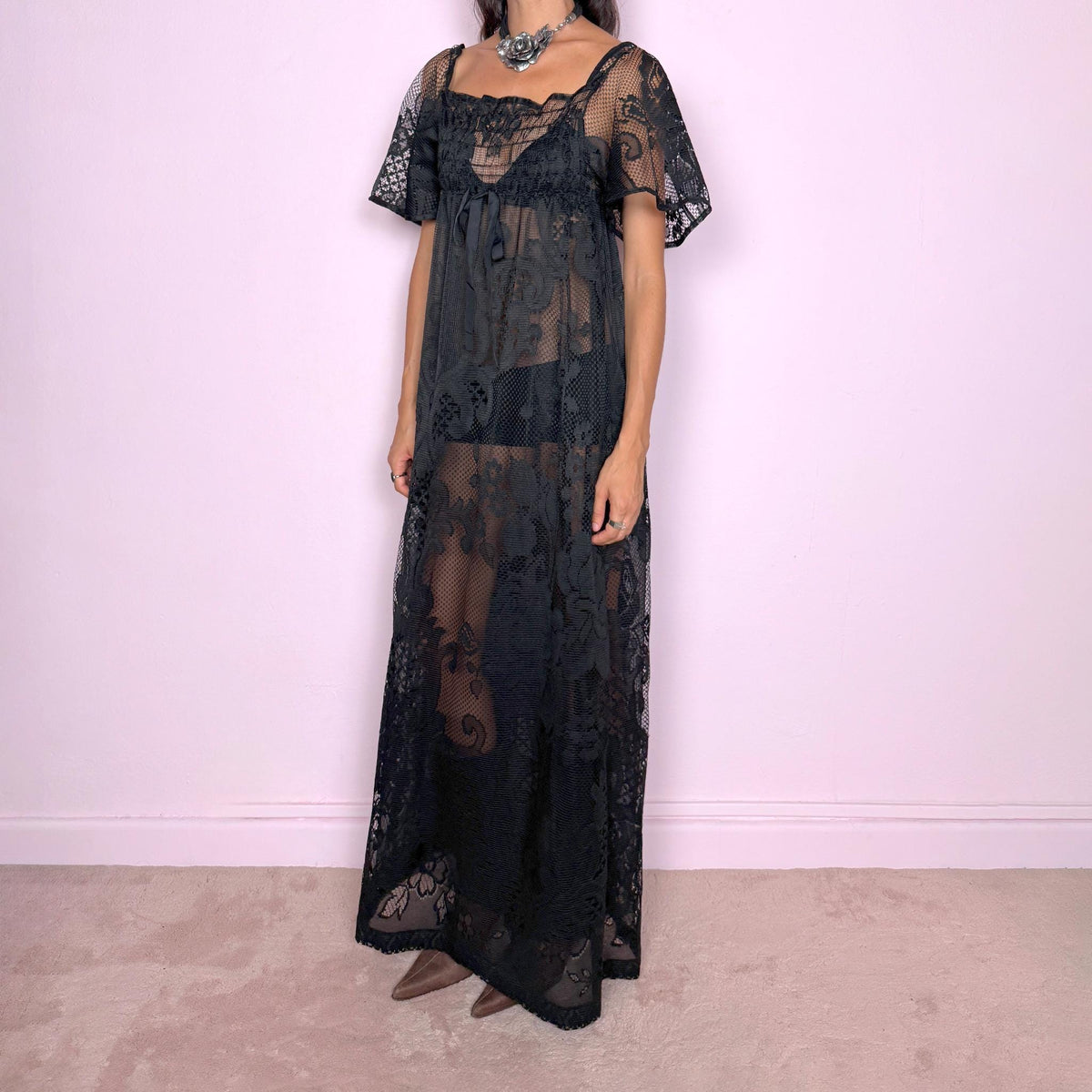 Vintage 90s black sheer lace maxi dress featuring an intricate all-over lace design with mixed floral and geometric motifs. Designed with a square neckline, softly gathered bust, short sheer sleeves, front tie detail, and a relaxed floor-length silhouette with a semi-sheer lining. For dark romantic styling and layered looks. The labels are missing, so the exact fabric is unknown. Excellent vintage condition.