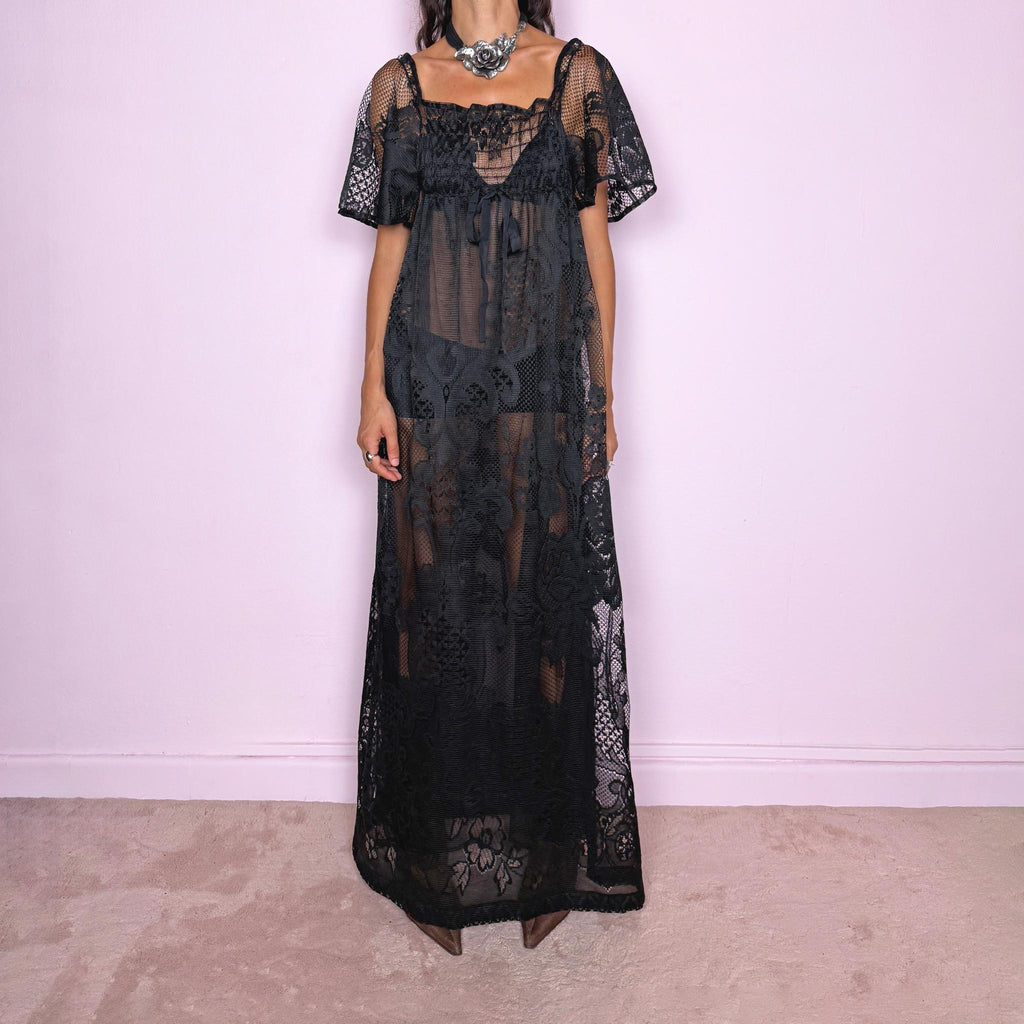 Vintage 90s black sheer lace maxi dress featuring an intricate all-over lace design with mixed floral and geometric motifs. Designed with a square neckline, softly gathered bust, short sheer sleeves, front tie detail, and a relaxed floor-length silhouette with a semi-sheer lining. For dark romantic styling and layered looks. The labels are missing, so the exact fabric is unknown. Excellent vintage condition.