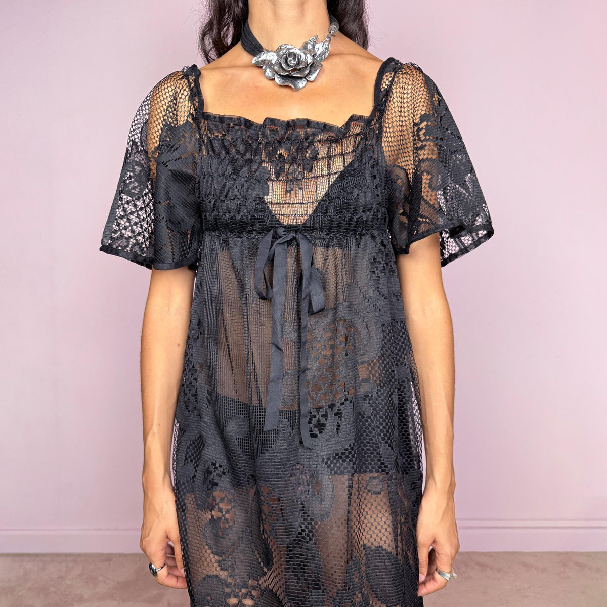 Vintage 90s black sheer lace maxi dress featuring an intricate all-over lace design with mixed floral and geometric motifs. Designed with a square neckline, softly gathered bust, short sheer sleeves, front tie detail, and a relaxed floor-length silhouette with a semi-sheer lining. For dark romantic styling and layered looks. The labels are missing, so the exact fabric is unknown. Excellent vintage condition.