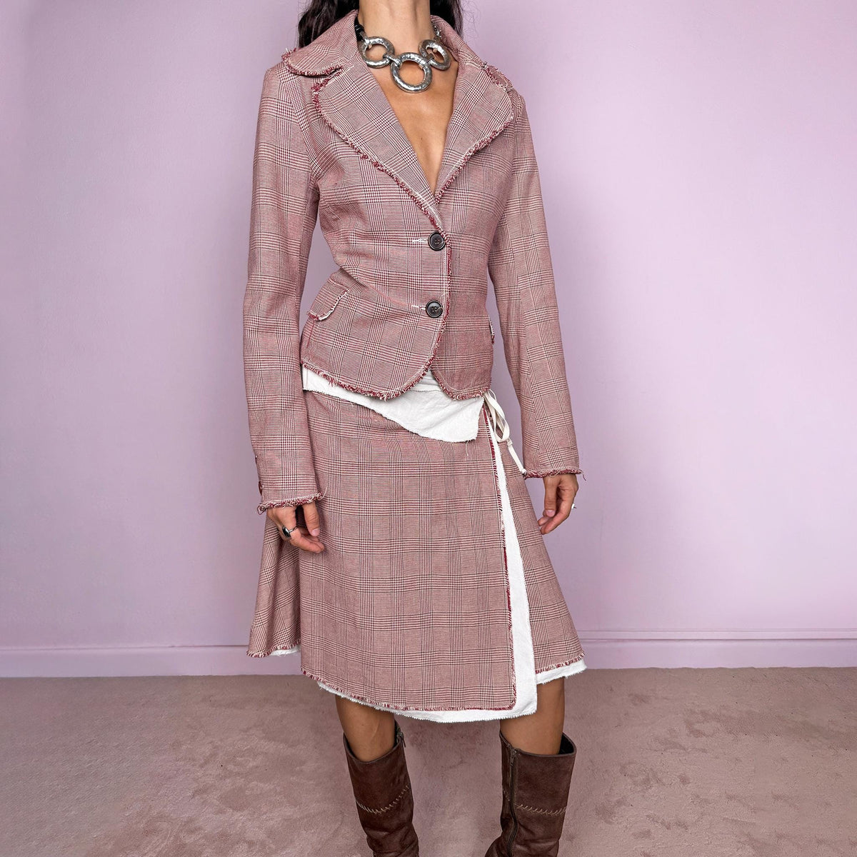 Vintage 2000s burgundy-red and cream two-piece skirt suit. The set includes a fitted blazer with a glen plaid / Prince of Wales check pattern, raw-edge trim, notched lapels, and a two-button front closure. Paired with a matching wrap-style midi skirt featuring layered cream lining, a side button closure, and an adjustable tie. The contrasting construction and unfinished edges create a relaxed, deconstructed feel while maintaining a tailored silhouette.