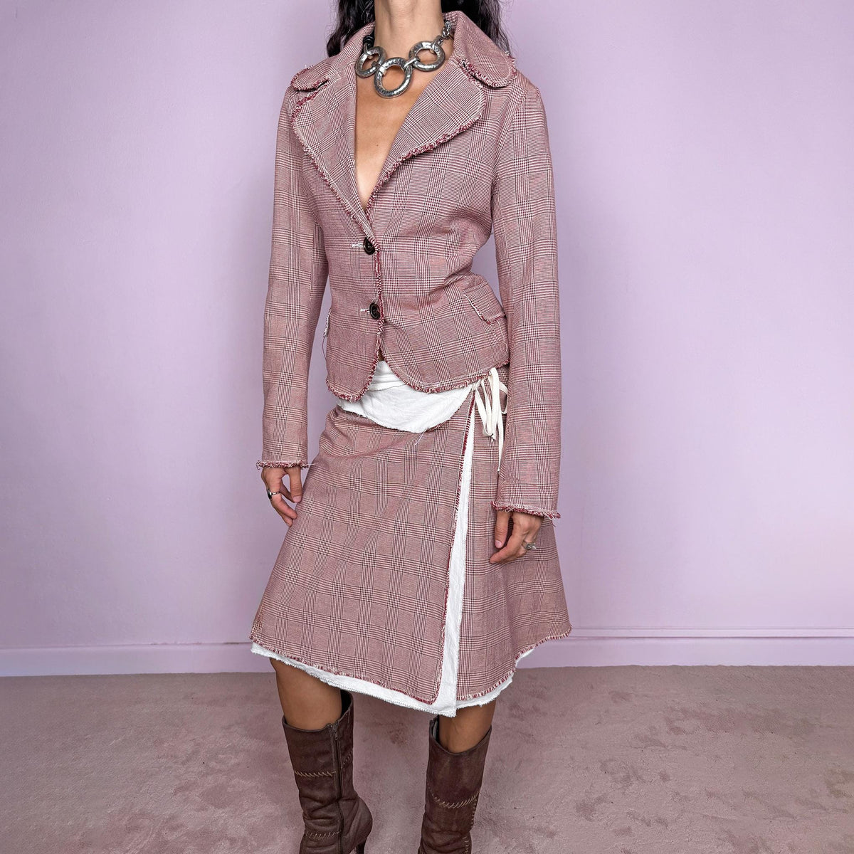 Vintage 2000s burgundy-red and cream two-piece skirt suit. The set includes a fitted blazer with a glen plaid / Prince of Wales check pattern, raw-edge trim, notched lapels, and a two-button front closure. Paired with a matching wrap-style midi skirt featuring layered cream lining, a side button closure, and an adjustable tie. The contrasting construction and unfinished edges create a relaxed, deconstructed feel while maintaining a tailored silhouette.