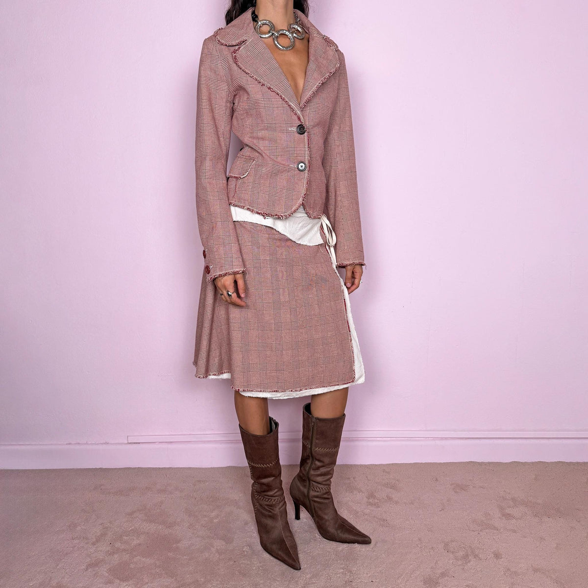 Vintage 2000s burgundy-red and cream two-piece skirt suit. The set includes a fitted blazer with a glen plaid / Prince of Wales check pattern, raw-edge trim, notched lapels, and a two-button front closure. Paired with a matching wrap-style midi skirt featuring layered cream lining, a side button closure, and an adjustable tie. The contrasting construction and unfinished edges create a relaxed, deconstructed feel while maintaining a tailored silhouette.