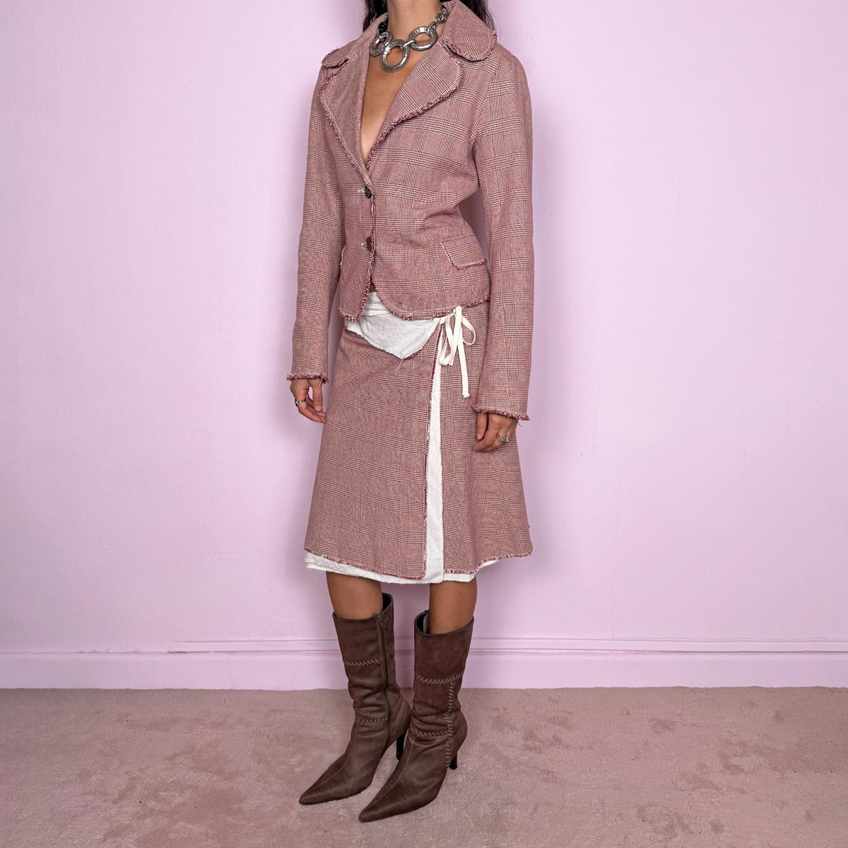 Vintage 2000s burgundy-red and cream two-piece skirt suit. The set includes a fitted blazer with a glen plaid / Prince of Wales check pattern, raw-edge trim, notched lapels, and a two-button front closure. Paired with a matching wrap-style midi skirt featuring layered cream lining, a side button closure, and an adjustable tie. The contrasting construction and unfinished edges create a relaxed, deconstructed feel while maintaining a tailored silhouette.