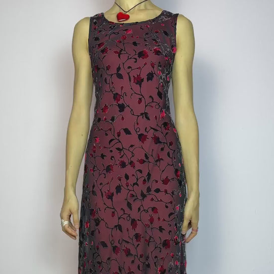The Vintage 90s Black Sheer Floral Midi Dress is a striking piece featuring a sheer black overlay with textured velvet floral details layered over a vibrant red lining. The sleeveless design and round neckline offer a timeless silhouette, while the fitted shape and midi length create a flattering, romantic look. The fabric is slightly stretchy and flowy, with a gothic romantic vibe perfect for dark fairycore, witchy looks, or 2000s party aesthetics. Excellent vintage condition.