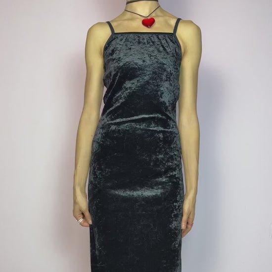 The Vintage 90s Black Velvet Slip Dress is a minimalist goth dream crafted from soft, stretchy black velvet with a subtle shine. This slip-style piece features a sleek scoop neckline, delicate spaghetti straps, and a flattering, body-hugging fit. The midi length adds a timeless silhouette that’s both romantic and effortlessly edgy. Perfect for layering or wearing solo, this dress is a go-to for witchy glam, grunge nights, or 90s-inspired minimal looks. Made in Europe. Great vintage condition.