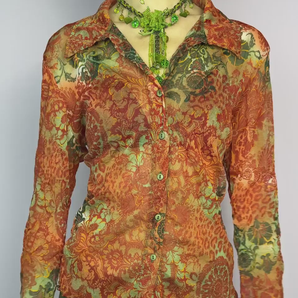 The Y2K Baroque Print Mesh Blouse is a vintage 2000s piece featuring a semi-sheer mesh fabric with a rich baroque-inspired floral print in warm tones. Designed with a fitted silhouette, button-up front, delicate lace trim on the cuffs and three quarter sleeves, the lightweight and stretchy fabric make it ideal for summer bohemian-inspired looks.