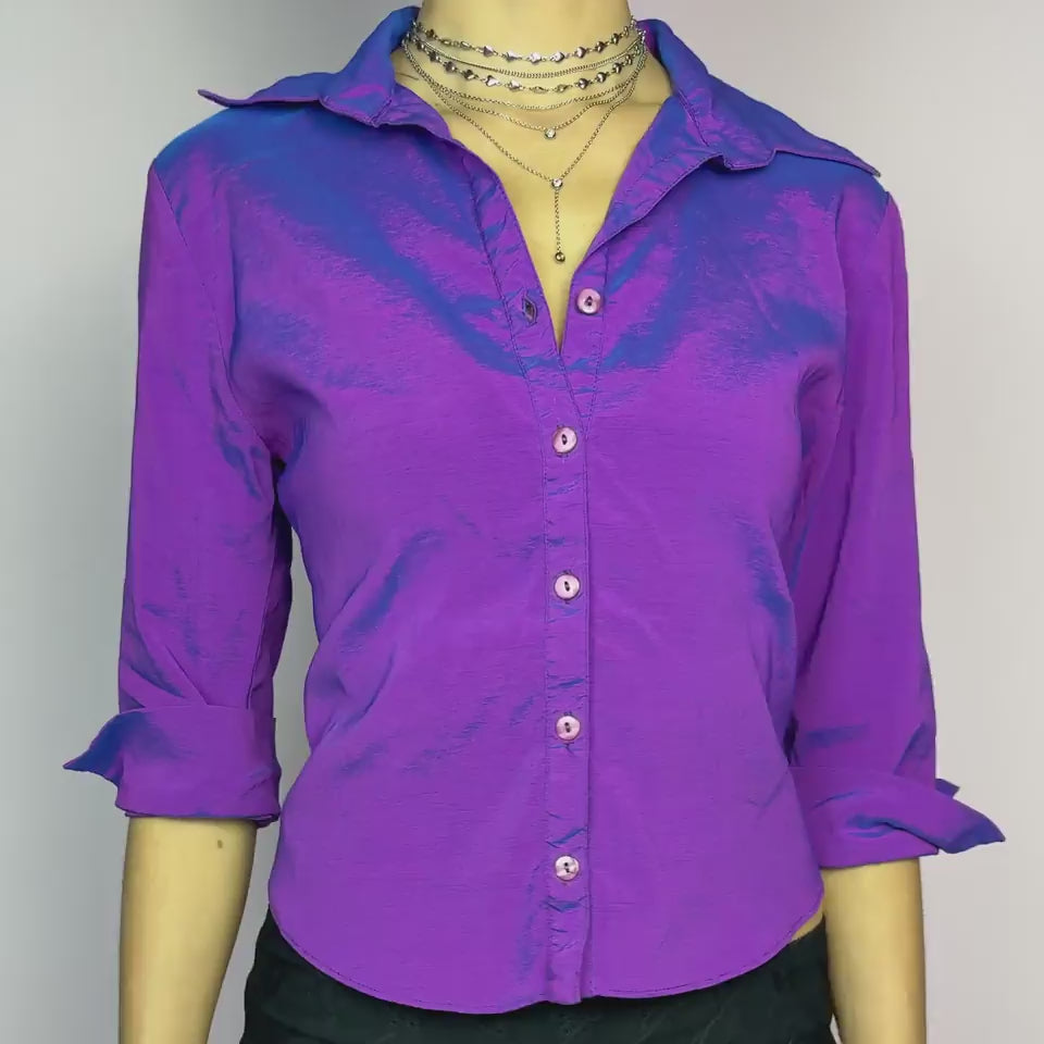 The Y2K Purple Iridescent Blouse is a vintage 2000s button-up top featuring a shimmery, iridescent stretchy fabric that shifts between purple and blue tones depending on the light. Designed with a structured collar, a fitted silhouette, and rolled-up 3/4 sleeves for a casual-chic look. Perfect for night outs and parties.