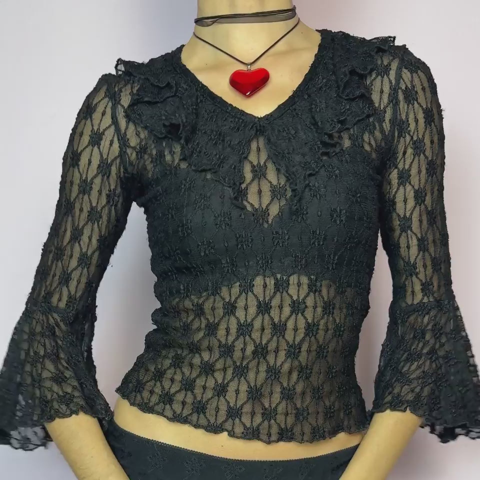 The Y2K Lace Ruffle Black Top is a vintage 2000s sheer black lace top featuring a fitted silhouette, mini ruffle details along the neckline, and flared three-quarter bell sleeves. The textured floral lace adds a romantic gothic touch, perfect for layering or wearing on its own. Ideal for summer night looks and festival outfits. Great vintage condition.