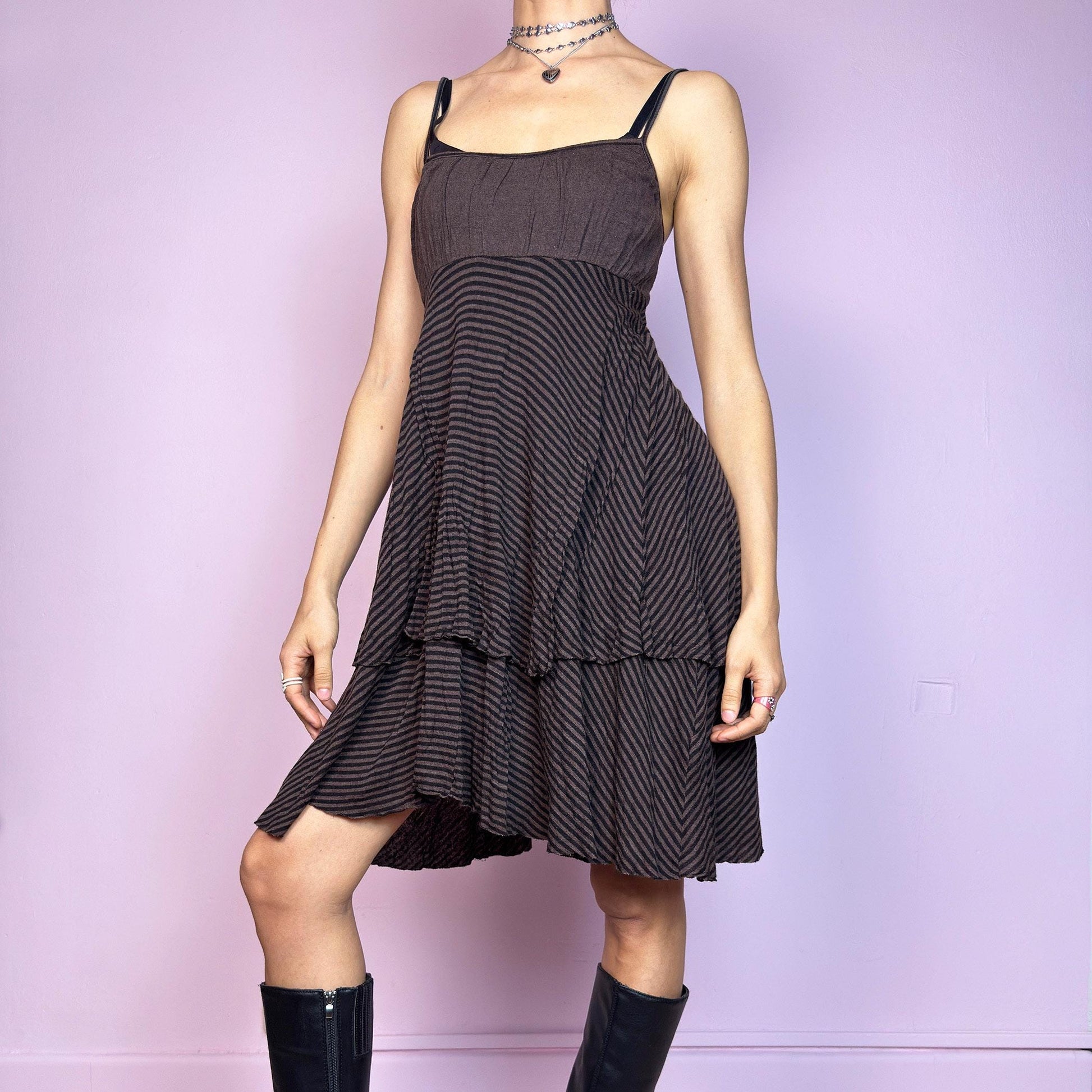 This vintage 2000s brown midi dress features a fine black stripe pattern, square neckline, and thin shoulder straps. Made from a soft, stretchy knit, it has an empire waist and a tiered asymmetric hem that drapes with ease. Perfect for summer. A casual, fairy grunge–inspired piece with subtle volume and flow—blending comfort, minimalism, and quiet edge. Great vintage condition.
