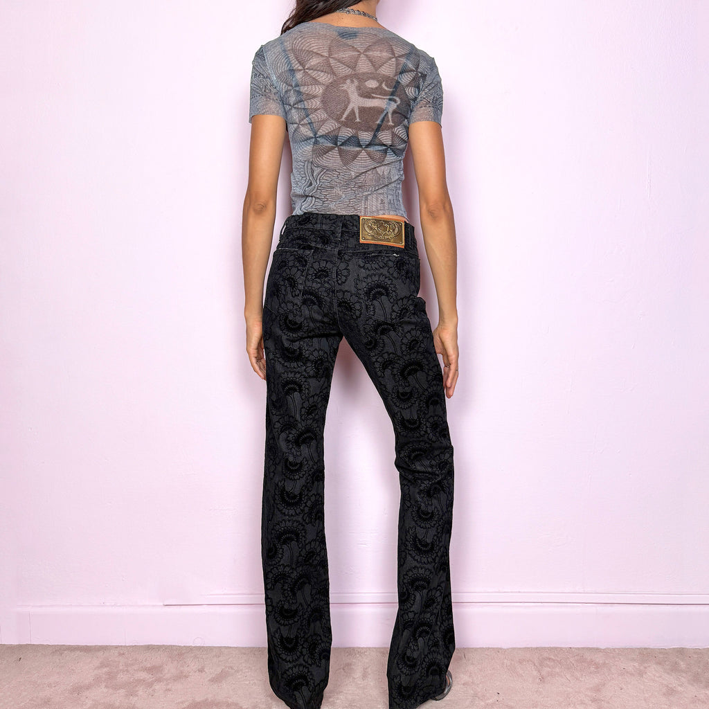 These vintage 2000s black straight jeans by Italian designer Roberto Cavalli for Just Cavalli feature a mid-rise fit and sleek straight-leg cut. Crafted from a cotton–polyester blend with slight stretch, they’re adorned with a devoré-style velvet floral pattern, blending elegance with Y2K edge. Detailed with front and back pockets, gold logo plaque, and zipper closure—ideal for night outings or elevated casual wear. Excellent vintage condition.