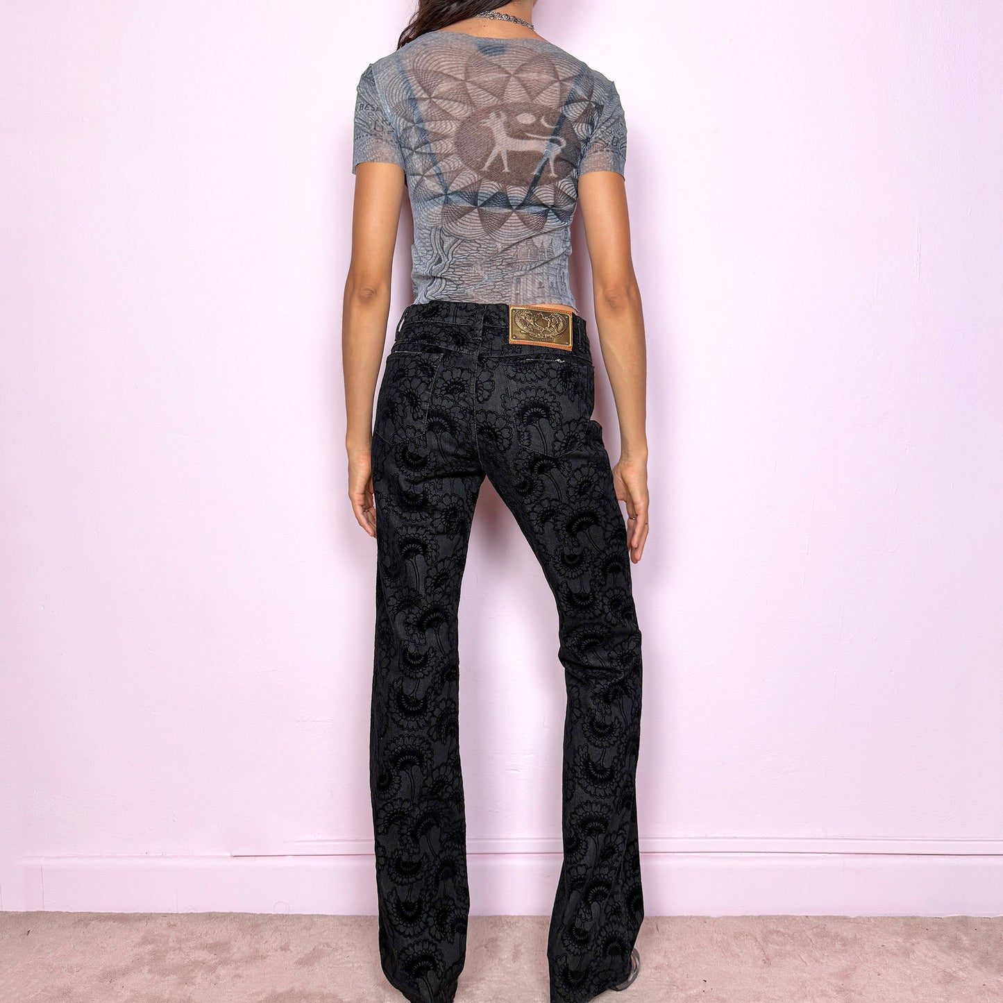 These vintage 2000s black straight jeans by Italian designer Roberto Cavalli for Just Cavalli feature a mid-rise fit and sleek straight-leg cut. Crafted from a cotton–polyester blend with slight stretch, they’re adorned with a devoré-style velvet floral pattern, blending elegance with Y2K edge. Detailed with front and back pockets, gold logo plaque, and zipper closure—ideal for night outings or elevated casual wear. Excellent vintage condition.