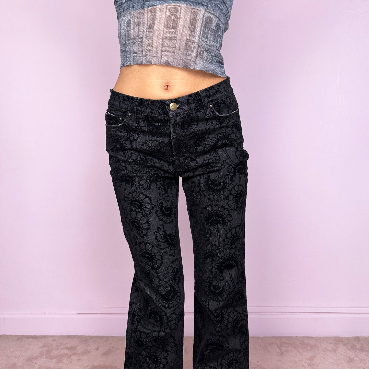 These vintage 2000s black straight jeans by Italian designer Roberto Cavalli for Just Cavalli feature a mid-rise fit and sleek straight-leg cut. Crafted from a cotton–polyester blend with slight stretch, they’re adorned with a devoré-style velvet floral pattern, blending elegance with Y2K edge. Detailed with front and back pockets, gold logo plaque, and zipper closure—ideal for night outings or elevated casual wear. Excellent vintage condition.