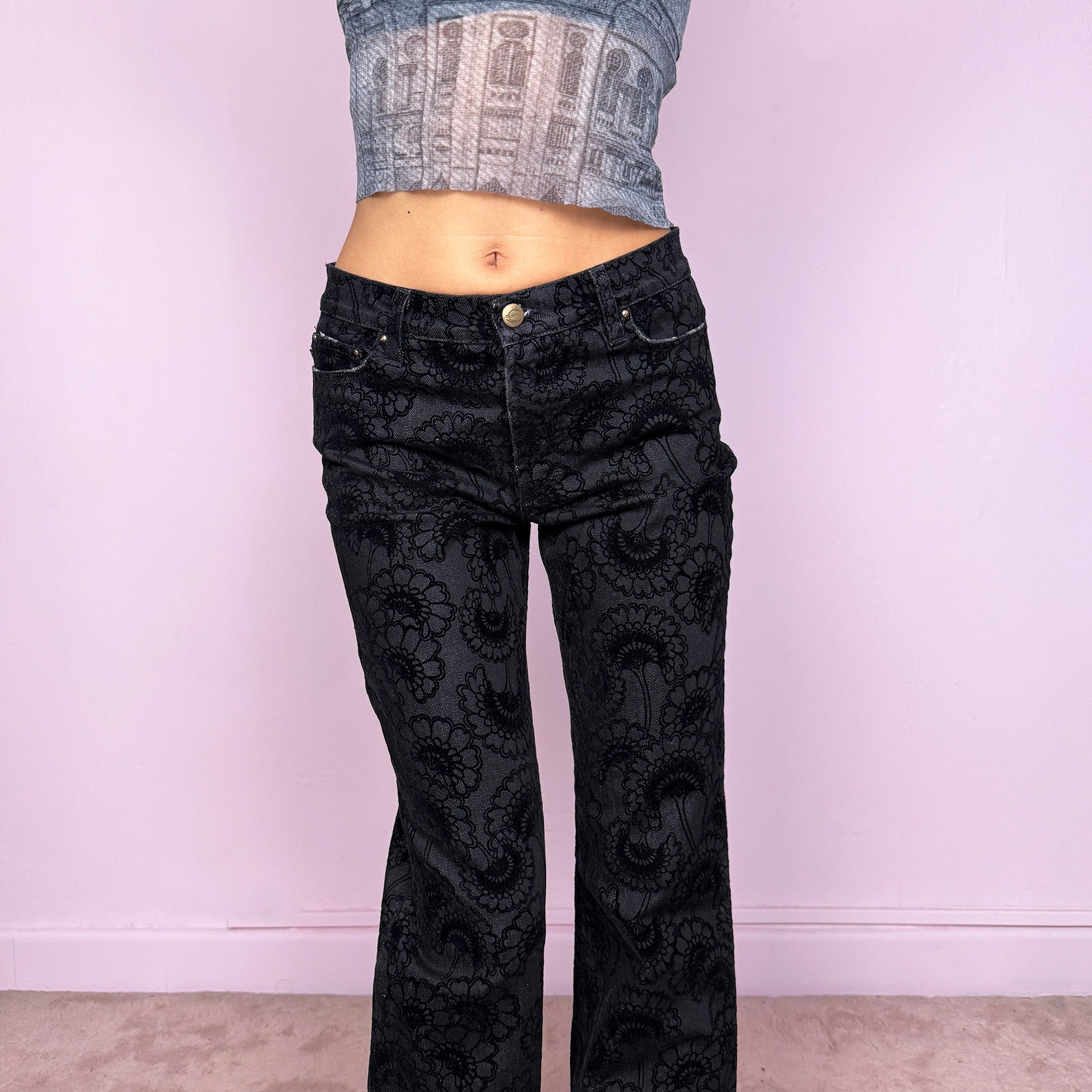 These vintage 2000s black straight jeans by Italian designer Roberto Cavalli for Just Cavalli feature a mid-rise fit and sleek straight-leg cut. Crafted from a cotton–polyester blend with slight stretch, they’re adorned with a devoré-style velvet floral pattern, blending elegance with Y2K edge. Detailed with front and back pockets, gold logo plaque, and zipper closure—ideal for night outings or elevated casual wear. Excellent vintage condition.